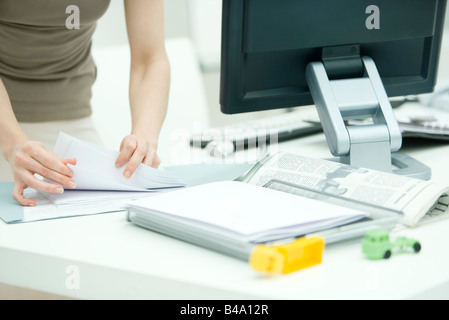 Ordinamento della donna attraverso i documenti sulla scrivania, per bambini giocattoli in primo piano, vista ritagliata Foto Stock