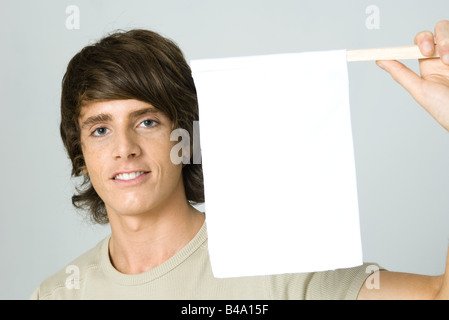 Giovane uomo mantenendo la bandiera bianca, sorridente in telecamera Foto Stock