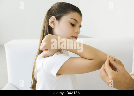 L'uomo mettendo bendaggio adesivo sulla ragazza del gomito, vista ritagliata Foto Stock