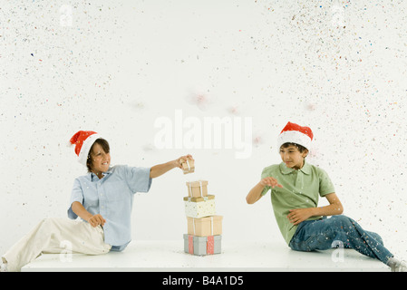 Due ragazzi indossando cappelli di Babbo Natale presenta di impilamento, coriandoli cadere intorno a loro Foto Stock