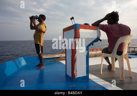 Utilizzando il binocolo per avvistare i tonni albacora sul ponte superiore a bordo di un tradizionale dhoni barca da pesca sull'Oceano Indiano, Maldive Foto Stock