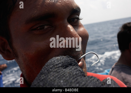 Un pescatore maldiviano mostra un gancio e guanto di maglia utilizzata per la linea di cattura per il tonno albacora di pesca a bordo di una barca dhoni, Oceano Indiano Foto Stock