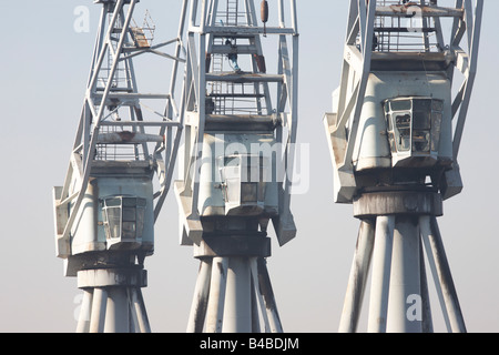 Tre bygone era gru portuali stare fermo nella nebbia mattutina, ridondante dopo decenni di movimentazione merci per la spedizione Foto Stock