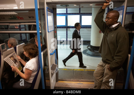 Un " commuter " di corsa a lunghe falcate passato le porte aperte di un treno dei pendolari in attesa di partenza da una piattaforma a Victoria station Foto Stock