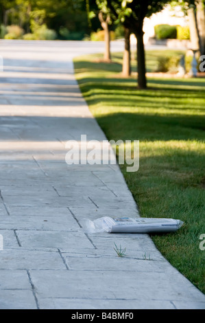 Quotidiano al mattino in polywrap sdraiato sul prato e il lungo viale di accesso alla casa suburbana Foto Stock