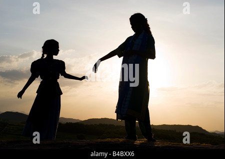 Due sorelle indiane danza su una roccia al tramonto silhouette. Andhra Pradesh, India Foto Stock