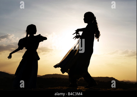 Due sorelle indiane eseguendo un indù danza devozionale su una roccia al tramonto silhouette. Andhra Pradesh, India Foto Stock