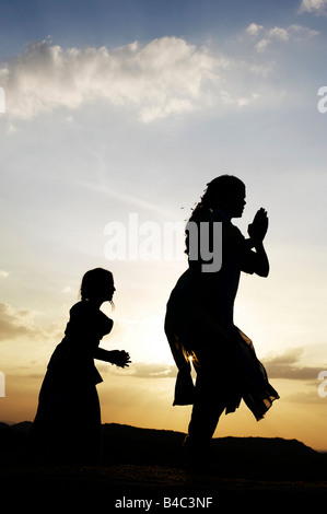 Due sorelle indiane eseguendo un indù danza devozionale su una roccia al tramonto silhouette. Andhra Pradesh, India Foto Stock