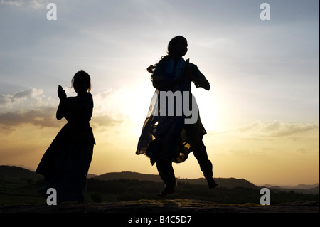 Due sorelle indiane eseguendo un indù danza devozionale su una roccia al tramonto silhouette. Andhra Pradesh, India Foto Stock