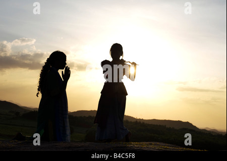 Due sorelle indiane eseguendo un indù danza devozionale su una roccia al tramonto silhouette. Andhra Pradesh, India Foto Stock