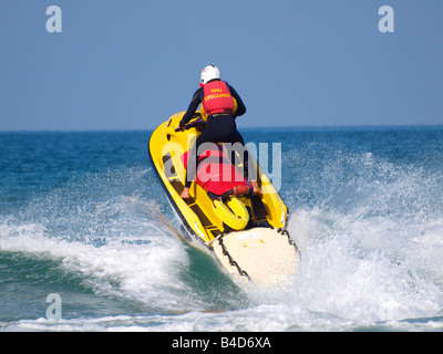 Bagnino RNLI su un rescue jetski schizzi attraverso un'onda Foto Stock
