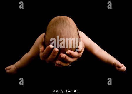 Vista della cima di la testa del bambino con le braccia spalancate come lei è stesa orizzontalmente nella madre con le mani in mano. Foto Stock