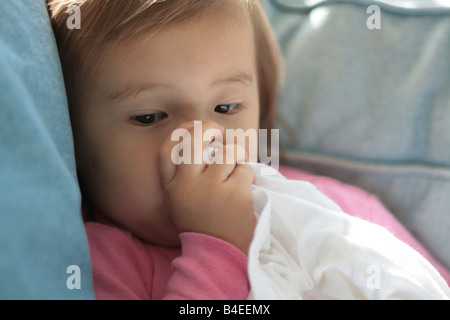 Una 17-mese-vecchia ragazza toddler aspira il suo pollice mentre si tiene un bianco tshirt che utilizza come una copertura di sicurezza. Foto Stock