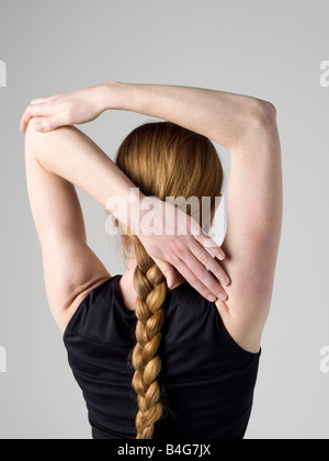 Una giovane donna qui di stiramento dei muscoli del braccio, vista posteriore Foto Stock