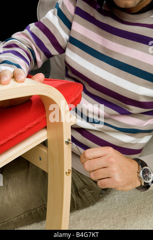 Un uomo utilizzando una chiave a brugola per il serraggio di una vite su una sedia Foto Stock