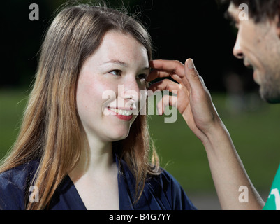 Un giovane uomo spingendo i capelli indietro da un giovane volto di donna Foto Stock