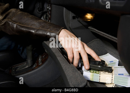 Una mano d'uomo afferrando una pistola da un vano portaoggetti piena di Unione europea valuta Foto Stock