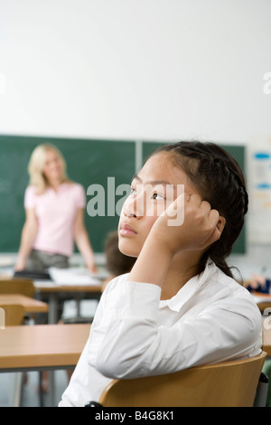 Un pre-adolescenti ragazza seduta nel retro di un'Aula cercando annoiato Foto Stock