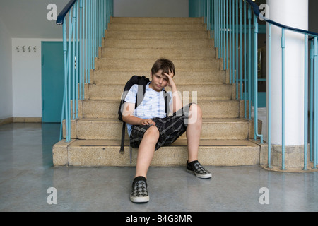 Un preoccupato pre-adolescenti ragazzo seduto sulle scale in una scuola Foto Stock