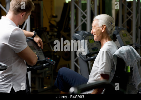 Un senior donna su una bicicletta stazionaria apprendimento da un istruttore Foto Stock