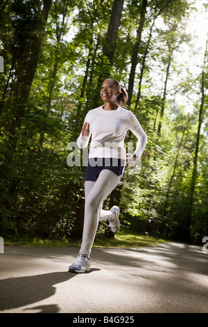 Una donna jogging attraverso il parco alberato Foto Stock