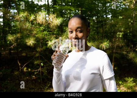 Una giovane donna in possesso di una bottiglia d'acqua in plastica, all'aperto Foto Stock