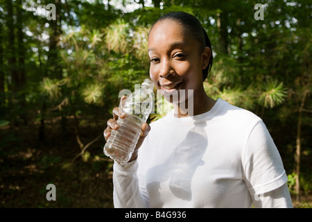 Una giovane donna in possesso di una bottiglia d'acqua in plastica, all'aperto Foto Stock