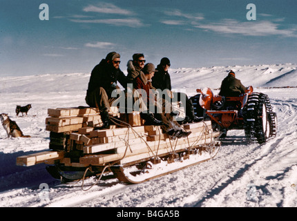 Il Trans Antarctic Expedition 1956 1958 Membri della spedizione team sedersi sulla parte superiore di una slitta sotto carico con il legno come un trattore tira a loro attraverso la neve esploratori soddisfare al Polo Sud i membri del team che sta tentando la prima superficie traversata dell'Antartico hanno aderito fino al Polo Sud il neozelandese Sir Edmund Hillary che ha già conquistato il Monte Everest è arrivato con il suo team 17 giorni fa presto questo pomeriggio Sir Edmund ha accolto con favore la squadra britannica guidata dal dottor coniglietto Vivian Fuchs al polo sud gli inglesi e Nuova Zelanda squadre sono membri di una comune Commonwealth Trans spedizione in Antartide Foto Stock