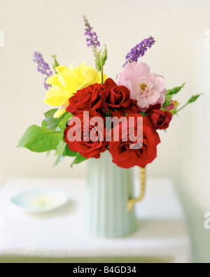 Rosa gialla e rose rosse in caraffa blu su un tavolo bianco Foto Stock