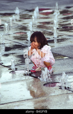 Bambina gioca in fontane schizzare fuori del pavimento di cemento. Foto Stock