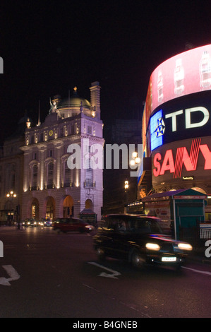 Sfocato black cab aziona attraverso Piccadilly sotto la pubblicità al neon di notte a Londra Foto Stock