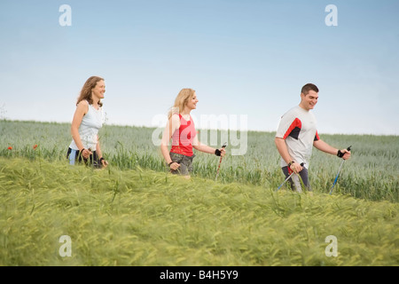 Profilo laterale di due donne e uomini in cammino con poli escursioni nel campo Foto Stock