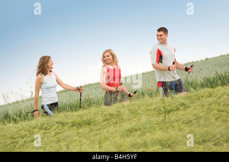 Profilo laterale di due donne e uomini in cammino con poli escursioni nel campo Foto Stock