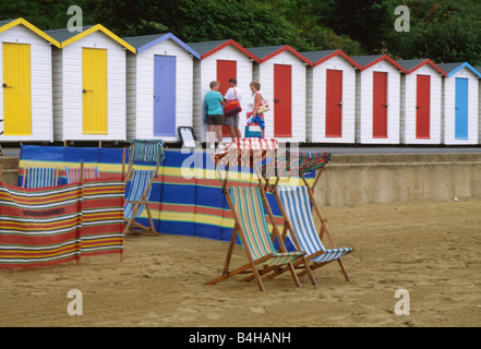 Striped sdraio frangiventi sulla spiaggia di sabbia di fronte delle colorate cabine in legno a Shanklin sull'Isola di Wight Foto Stock