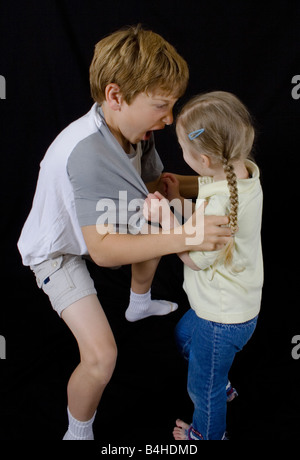 Ritratto a colori, due bambini, ragazza, boy, la lotta contro la rabbia di spinta affacciati su sfondo nero Foto Stock