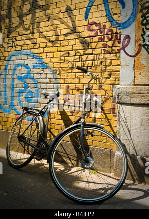 Un vecchio e ruggine tradizionale bicicletta olandese appoggiato contro una parete giallo coperto di graffiti a L'Aia, Paesi Bassi Foto Stock