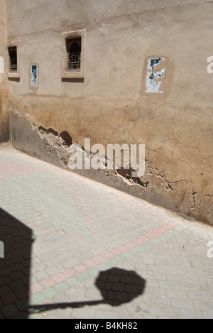 Una strada acciottolata a Marrakech, Marocco che mostra una parete danneggiata, alcuni fly poster e un forte ombra di una strada luce. Foto Stock