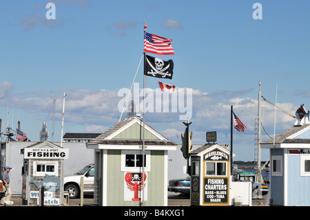 Fila di charter di pesca cabine biglietto sul molo con americani, canadesi e bandiere pirata sulla giornata di sole nel porto di Plymouth, MA USA Foto Stock