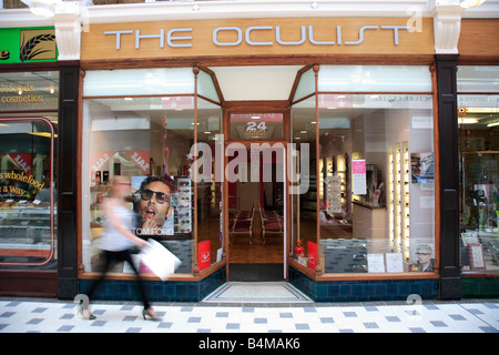 Donna oltrepassando un quartiere alla moda di High Street Opticians Shop Foto Stock