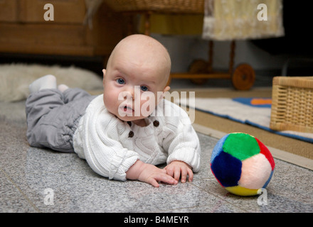 Bambino di 6 mesi di indossare una maglia bianca pullover e pantaloni grigi giace su un piano di marmo nella parte anteriore di un colorato palla di peluche Foto Stock