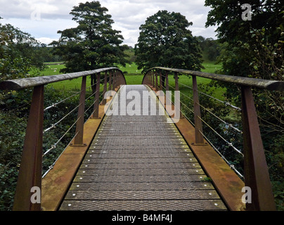 Vista su metallo arrugginito ponte che conduce in campi aperti in campagna boscosa in Cumbria Inghilterra settentrionale Foto Stock