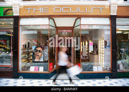 Donna oltrepassando un quartiere alla moda di High Street Opticians Shop Foto Stock