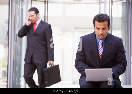 Imprenditore all'aperto di fronte all edificio utilizzando laptop con imprenditore è in esecuzione in background (alta chiave/messa a fuoco selettiva) Foto Stock