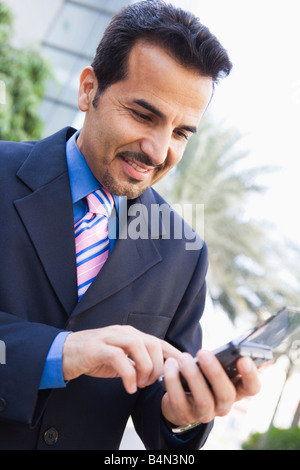 Imprenditore all'aperto utilizzando assistente digitale personale e sorridente (alta chiave/messa a fuoco selettiva) Foto Stock