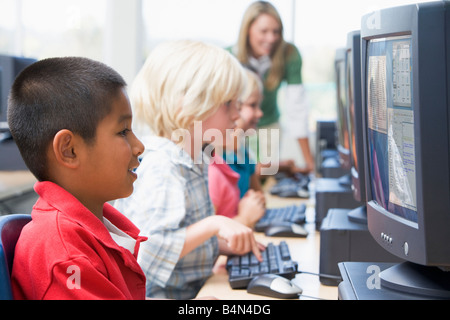 Quattro figli a terminali di computer con insegnante in background (profondità di campo/high key) Foto Stock