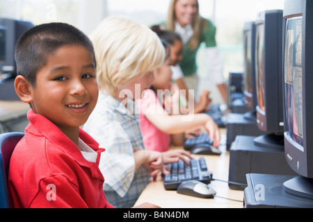 Quattro figli a terminali di computer con insegnante in background (profondità di campo/high key) Foto Stock