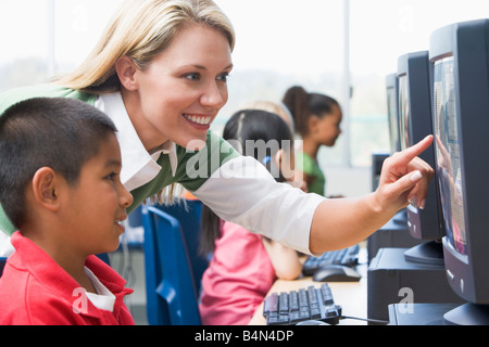 Docente aiutare lo studente a terminale di computer con gli studenti di sfondo (il fuoco selettivo/high key) Foto Stock