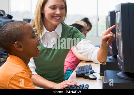 Docente aiutare lo studente a terminale di computer con gli studenti di sfondo (il fuoco selettivo/high key) Foto Stock