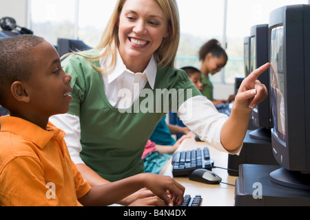 Docente aiutare lo studente a terminale di computer con gli studenti di sfondo (il fuoco selettivo/high key) Foto Stock