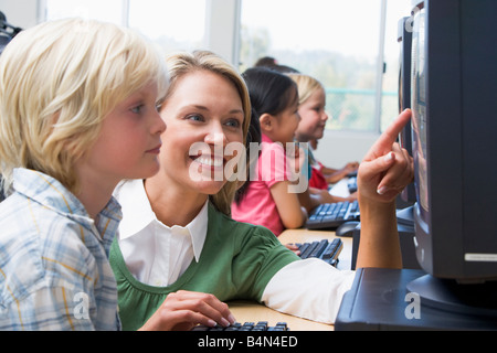 Docente aiutare lo studente a terminale di computer con gli studenti in background (profondità di campo/high key) Foto Stock